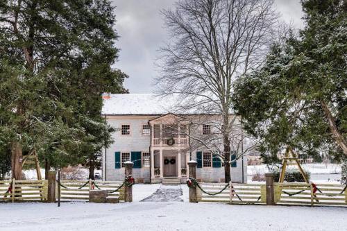 A historic house surrounded by snow, with green shutters and festive decorations on the gate, under a cloudy sky.