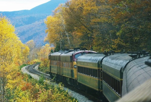 A vintage train winds through a colorful autumn landscape with vibrant yellow and orange foliage.