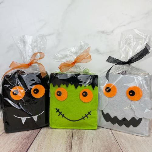 Three Halloween-themed gift boxes: a black vampire, a green monster, and a gray ghost, all wrapped in clear cellophane.