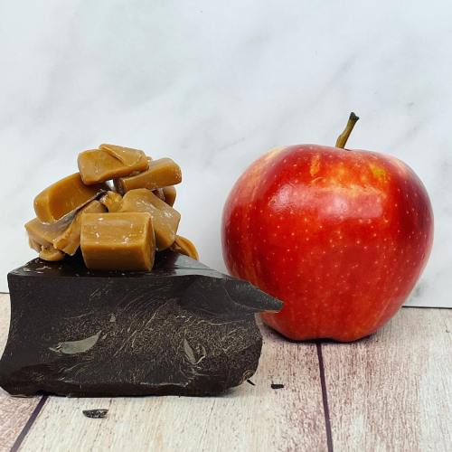 A shiny red apple next to a stack of caramel pieces on a dark surface.