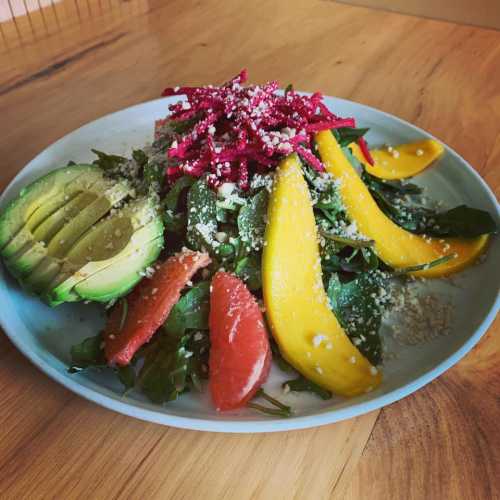 A colorful salad with avocado, mango, beets, greens, and sprinkled cheese on a white plate.