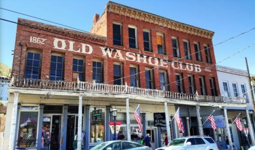 Historic Old Washoe Club building with red brick facade, large windows, and American flags, set against a clear blue sky.