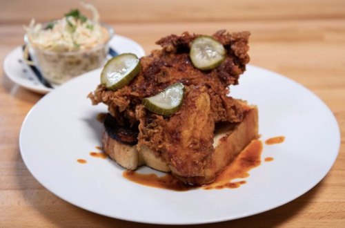 A plate featuring fried chicken on toast, topped with pickles, alongside a small bowl of coleslaw.