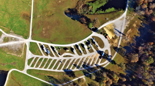 Aerial view of a park with neatly arranged RV parking spaces and surrounding green fields and trees.