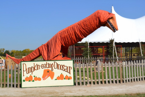 A large, orange dinosaur sculpture made of fabric, standing next to a sign that reads "Pumpkin-eating Dinosaur."