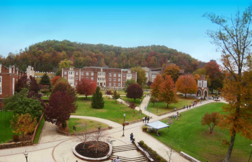 A scenic view of a college campus with autumn foliage, pathways, and buildings against a backdrop of rolling hills.