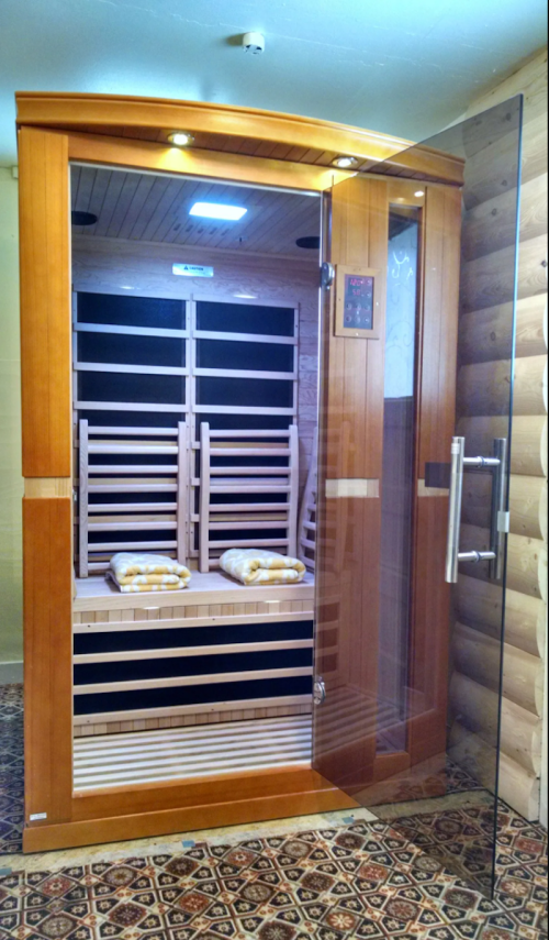 A wooden sauna with benches and neatly folded towels, featuring a glass door and warm lighting.
