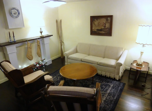 Cozy living room with a sofa, two chairs, a round table, and a fireplace decorated for the holidays.
