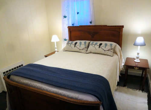 Cozy bedroom featuring a wooden bed, decorative pillows, bedside lamps, and a window with sheer curtains.