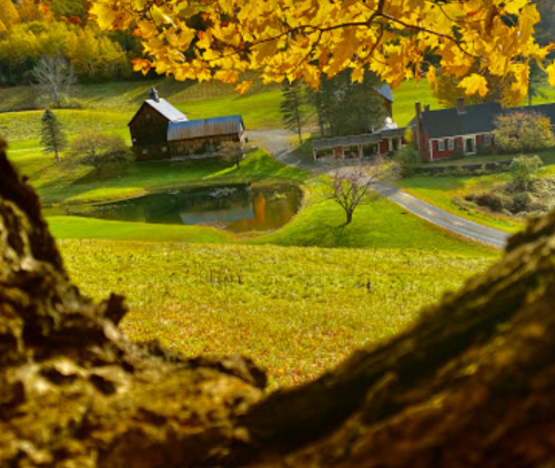 A scenic view of a rural landscape with autumn foliage, a pond, and charming farmhouses in the distance.