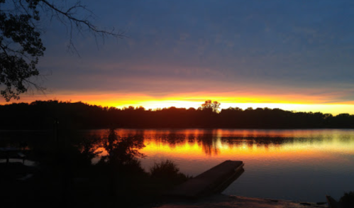 A serene sunset over a calm lake, with vibrant orange and yellow hues reflecting on the water's surface.