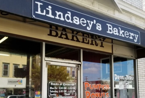 Sign for Lindsey's Bakery with hours of operation and a display for pumpkin donuts, featuring a drive-thru.
