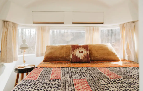 Cozy bedroom with a patterned blanket, decorative pillows, and large windows letting in natural light.