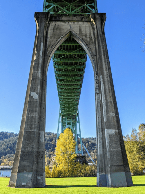 View from beneath a green bridge arch, with a clear blue sky and trees in the background.