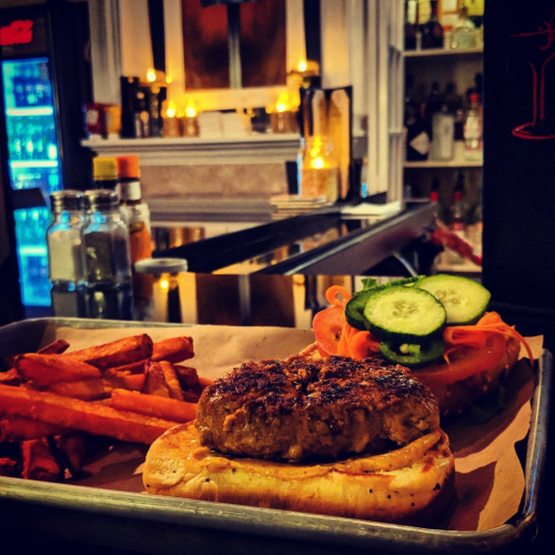 A plate with a burger, sliced cucumbers, and sweet potato fries, set in a cozy, dimly lit restaurant.