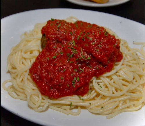 A plate of spaghetti topped with marinara sauce and herbs, served with a meatball.