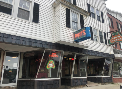 Exterior of Pat's Pizza, featuring a sign and large windows, located in a multi-story building with a classic design.