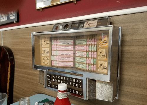 A vintage jukebox mounted on a wall, featuring colorful song selection cards and a classic design.