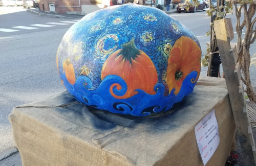 A large, painted rock featuring swirls of blue, pumpkins, and a starry night design, displayed on a burlap-covered base.