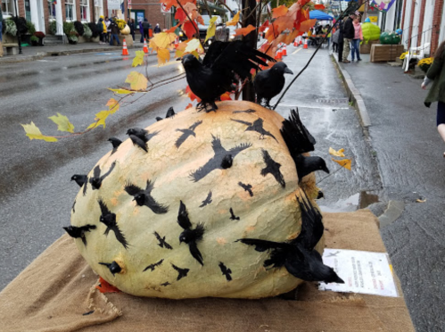 A large pumpkin decorated with black birds, set on a street during a festive event.