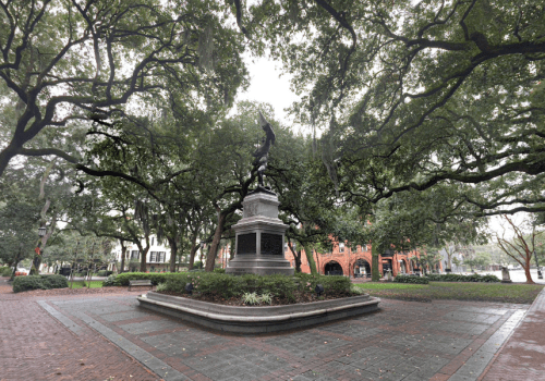 A statue surrounded by trees in a park, with brick pathways and buildings in the background.