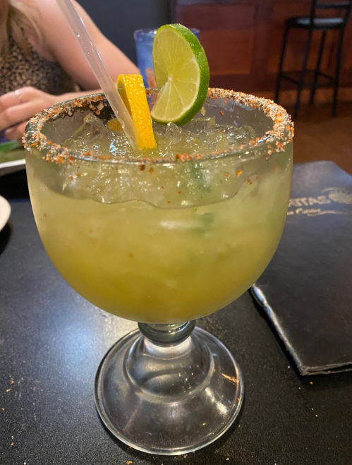 A large margarita in a glass with a salted rim, garnished with lime and orange slices.