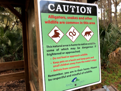 Sign warning about alligators, snakes, and wildlife; advises on safety and respect for animals in the area.