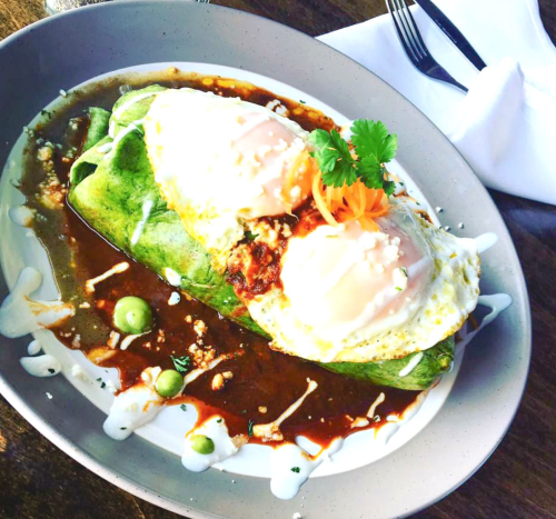 A plate of enchiladas topped with two poached eggs, drizzled with sauce and garnished with cilantro and carrots.