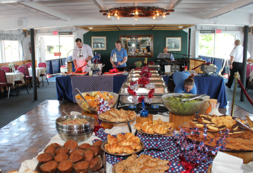 A buffet spread with various dishes and desserts, with staff preparing food in a dining area on a boat.