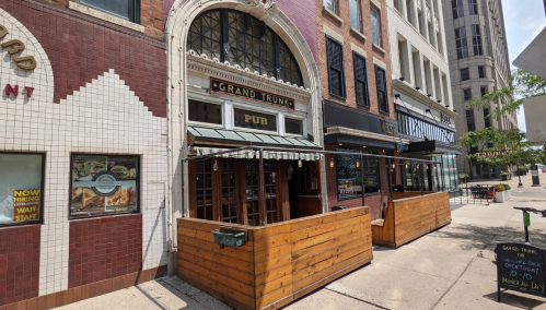 Exterior view of Grand Trunk Pub, featuring wooden seating and a brick facade in an urban setting.