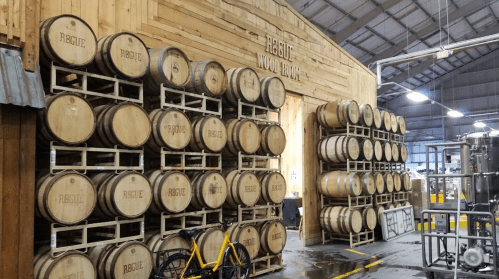Wooden barrels stacked against a wooden wall in a brewery, with a bicycle in the foreground.