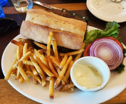 A plate with a sandwich, crispy fries, lettuce, onion slices, and a small bowl of dipping sauce.