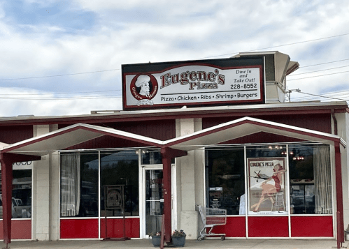 A restaurant exterior with a sign reading "Eugene's Pizza," offering pizza, chicken, ribs, shrimp, and burgers.
