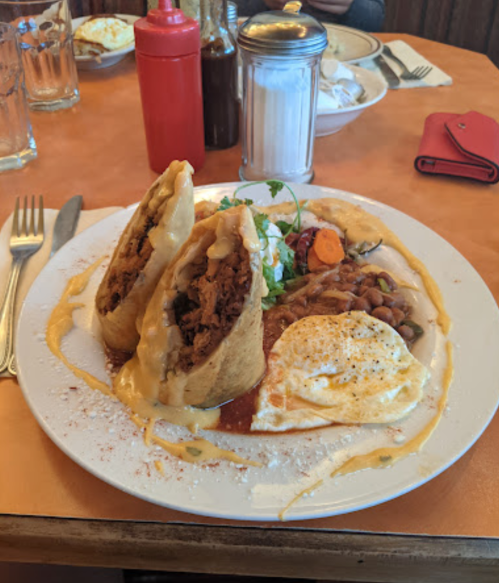 A plate of breakfast featuring two burritos, refried beans, a fried egg, and garnished with cilantro.