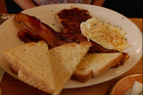 A plate with crispy bacon, a fried egg, hash browns, and slices of toasted bread.