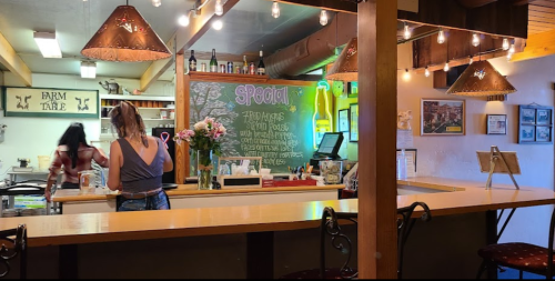 A cozy café interior with a counter, chalkboard specials, and warm lighting. Two people are engaged in activities.