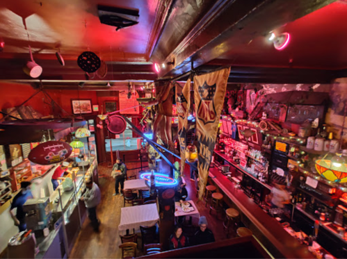 A cozy bar interior with colorful lights, vintage decor, and patrons enjoying drinks at tables.