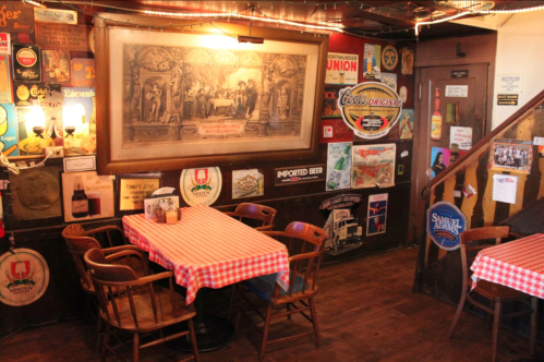 Cozy restaurant interior with checkered tablecloths, vintage beer signs, and a large framed artwork on the wall.
