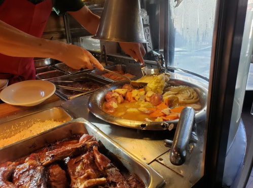 A person serving a plate of food from a buffet, featuring meats, vegetables, and rice in a restaurant setting.