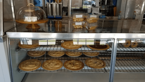 A display case filled with various pies, including fruit and cream varieties, in a bakery setting.