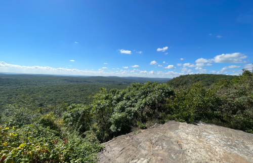 A panoramic view of lush green hills under a clear blue sky with scattered clouds.