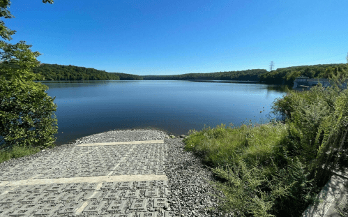 A serene lake view with clear blue skies, surrounded by lush greenery and a rocky shoreline.