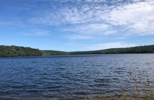 A serene lake surrounded by lush green hills under a partly cloudy blue sky.