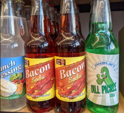 Four novelty soda bottles: ranch dressing, bacon (two flavors), and dill pickle, displayed on a shelf.