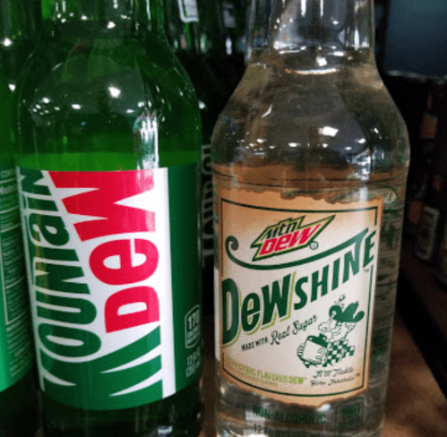 Two bottles of Mountain Dew: one green and one clear labeled "Dewshine," featuring a vintage design.