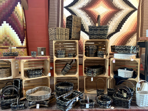 A display of various woven baskets arranged on wooden crates against a colorful quilt backdrop.