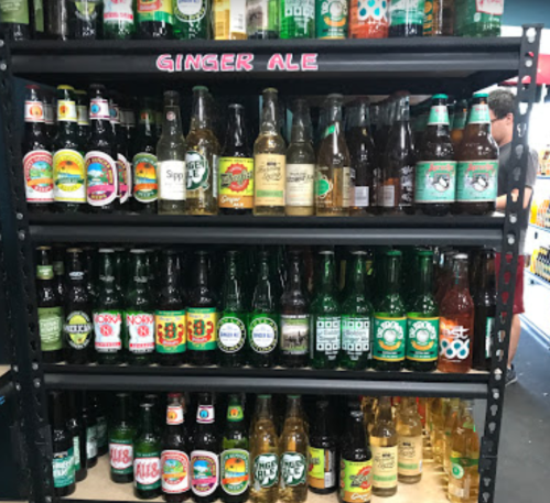 A display shelf filled with various brands of ginger ale and soda bottles in a store.