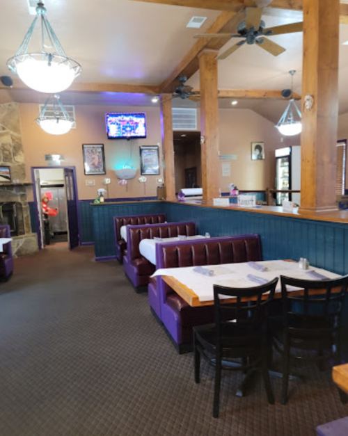 Interior of a restaurant featuring purple booths, wooden beams, and a cozy atmosphere with a bar in the background.
