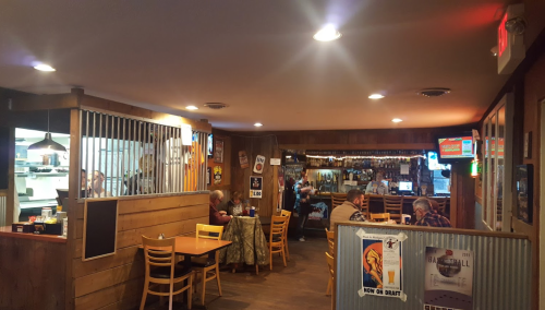 Cozy restaurant interior with wooden decor, tables, and patrons enjoying their meals. Warm lighting creates a welcoming atmosphere.