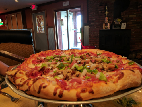 A large pizza topped with green peppers, mushrooms, and meats, served on a silver platter in a restaurant setting.